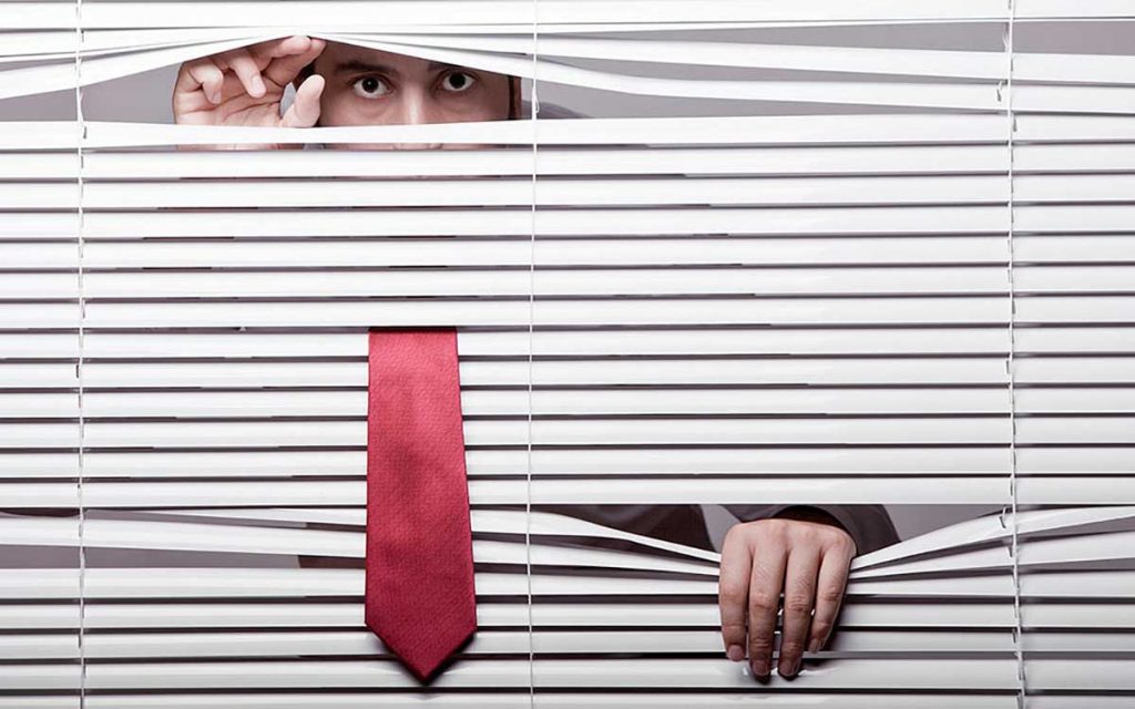 Man peeping through blinds because he is hiding.