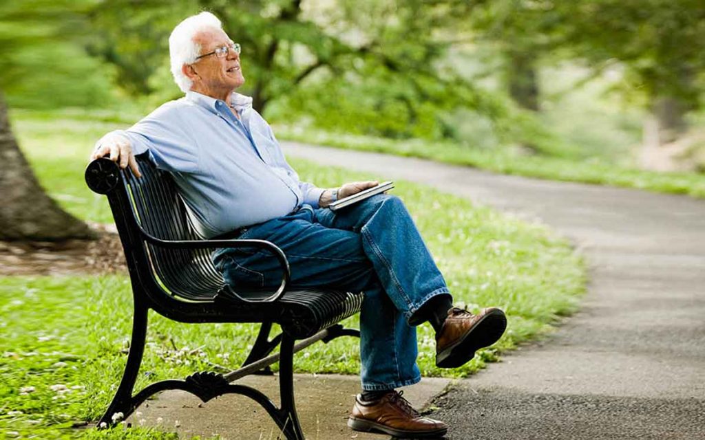Man relaxing on park bench and worry free with a hearing aid guide.