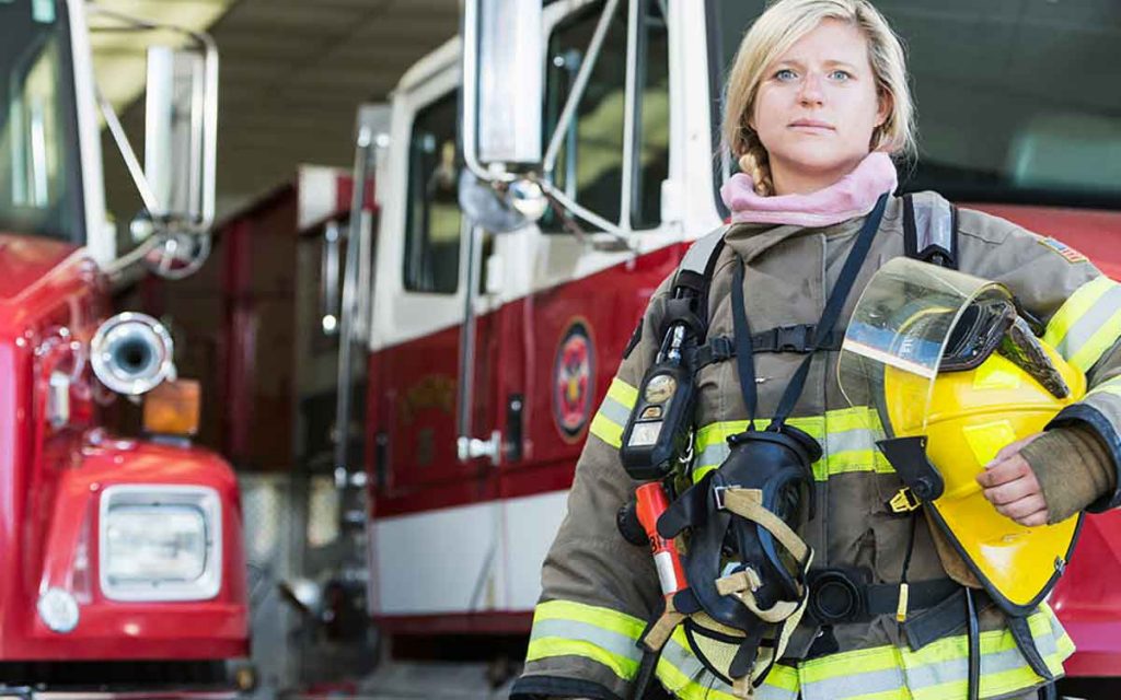 Woman firefighter in front of a fire station. Hearing loss can come from firetrucks.