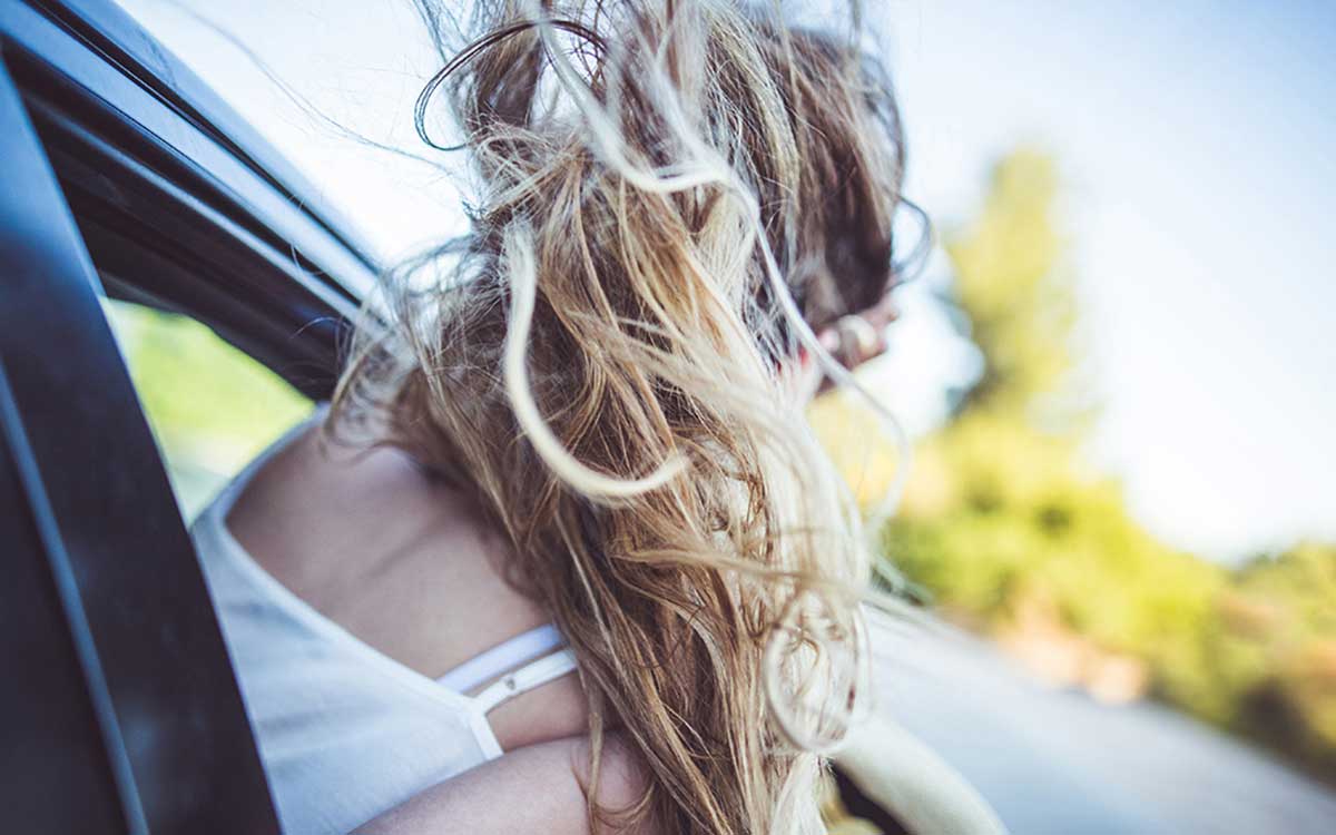 Woman with her head out the window of a car.