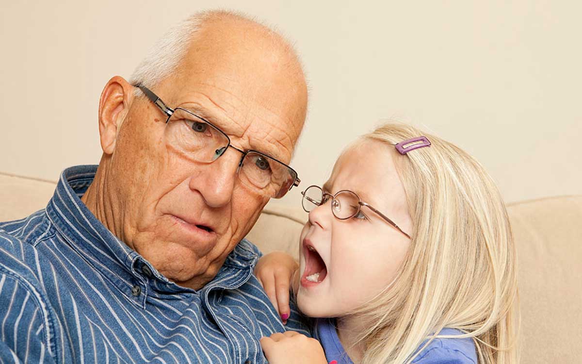 Elderly man suffering from single sided deafness leaning in to hear his grandaughter