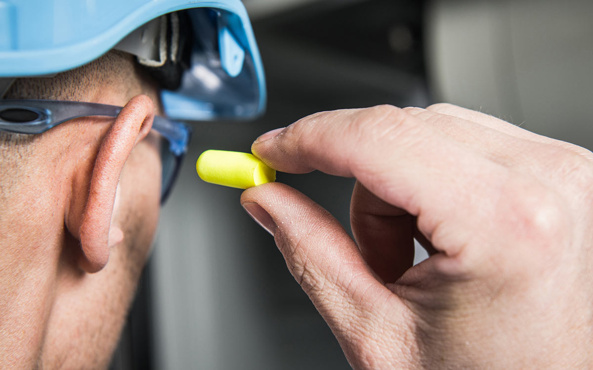 Man putting in ear plugs because of workplace noise.