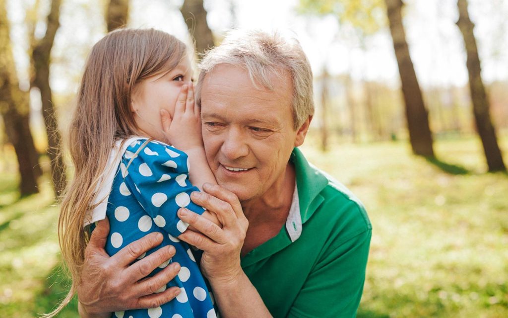 Man with granddaughter whispering into his ear. Comfortable hearing aids.