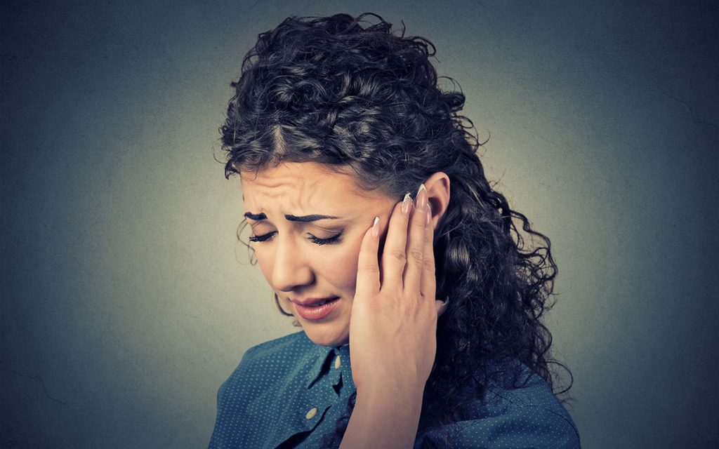 Woman holding her ear suffering from Pulsatile Tinnitus.