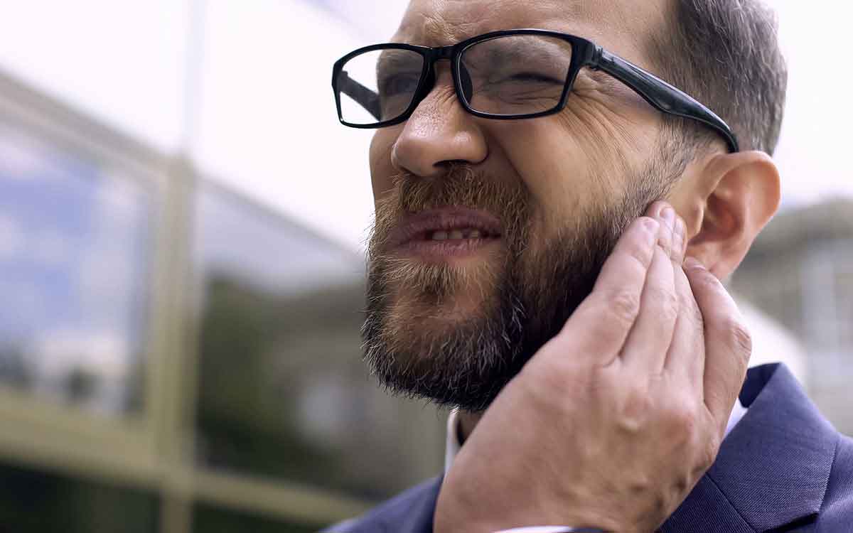 Man holding his ear because earwax is giving him hearing loss.