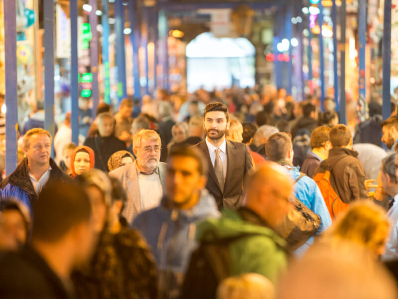Man with hearing loss in a grey suit standing in the middle of a busy marketplace unable to discern sounds.