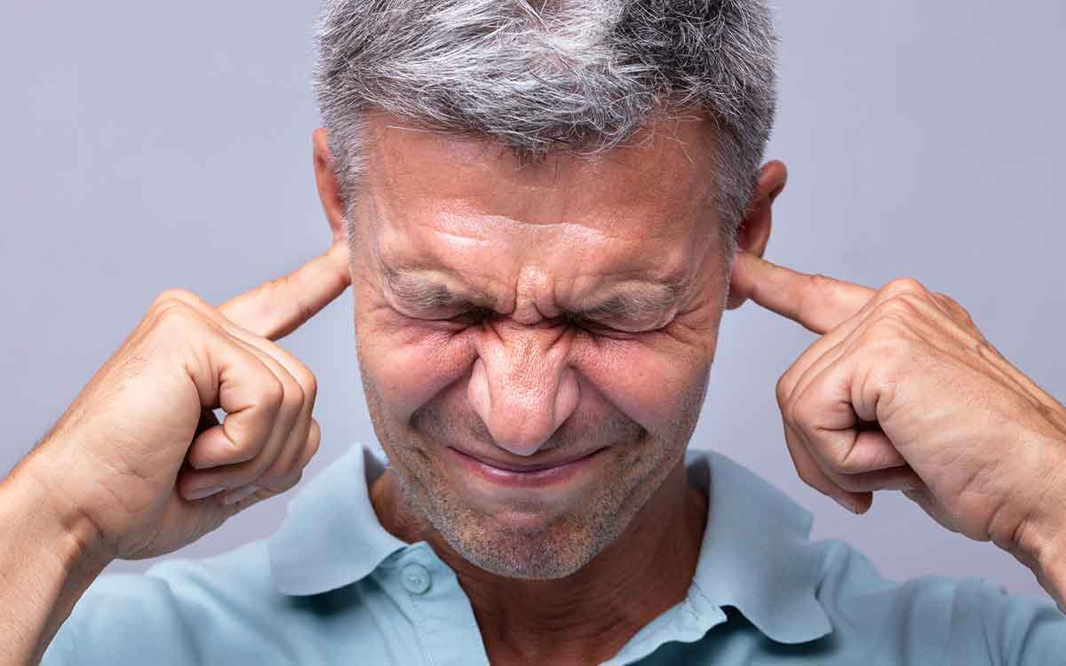 Man with his fingers in his ears blocked and causing hearing loss.