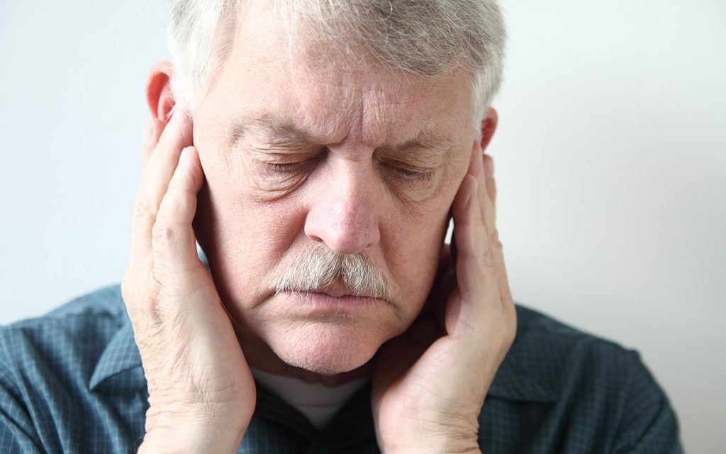 Man with his hands over his ears suffering from Tinnitus.