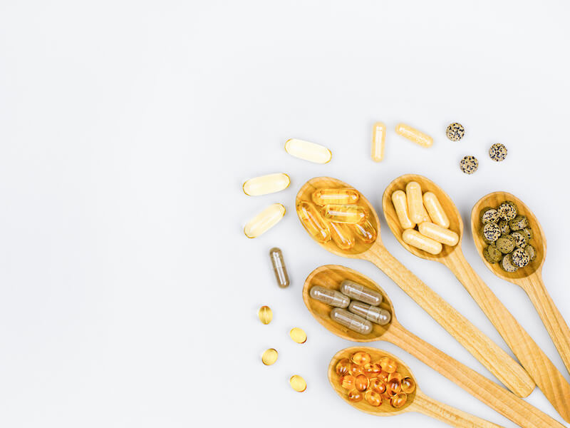 Mix of vitamins separated into different wooden spoons on a white background.