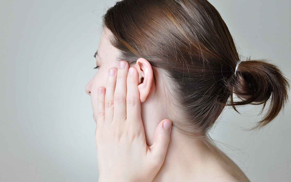 Woman with hand over her ear suffering from Tinnitus.