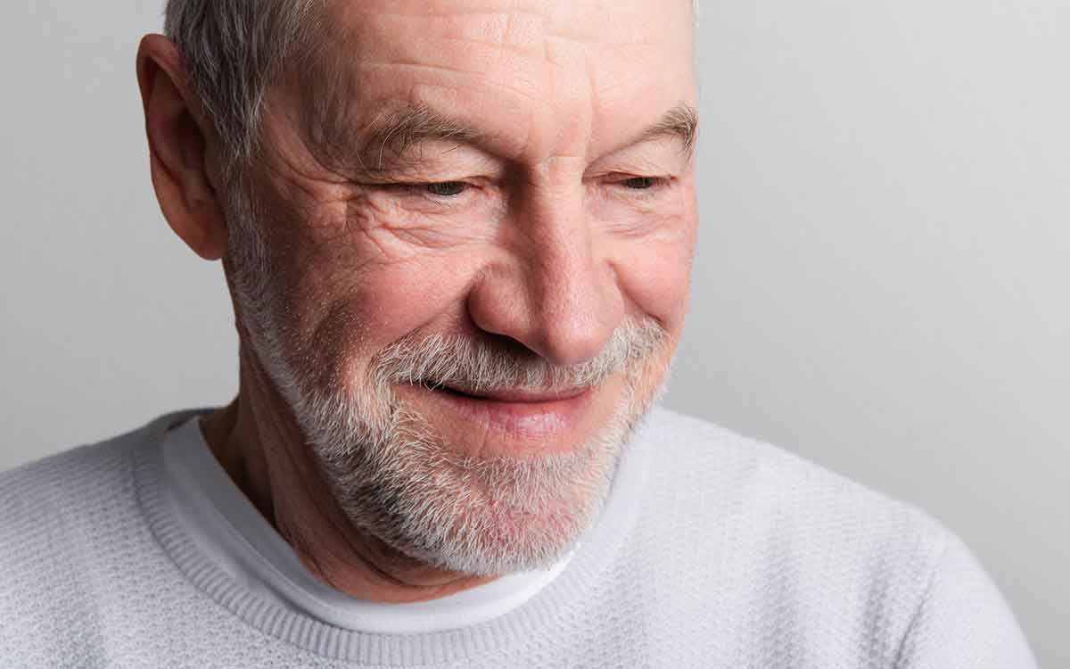 Portrait of a happy senior man with beard and mustache in a studio who is preventing aging with hearing aids.