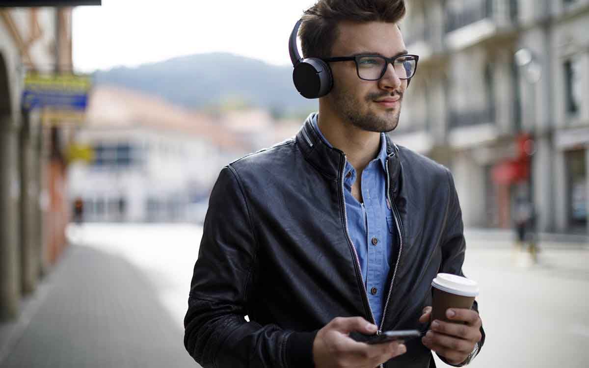 Smiling young man listening to music and drinking coffee outdoors listing to his headphones.