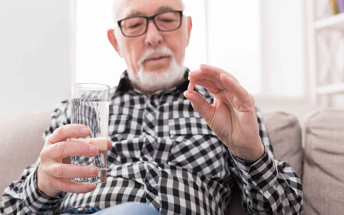 Senior man having a glass of water and pills in hand for Tinnitus.