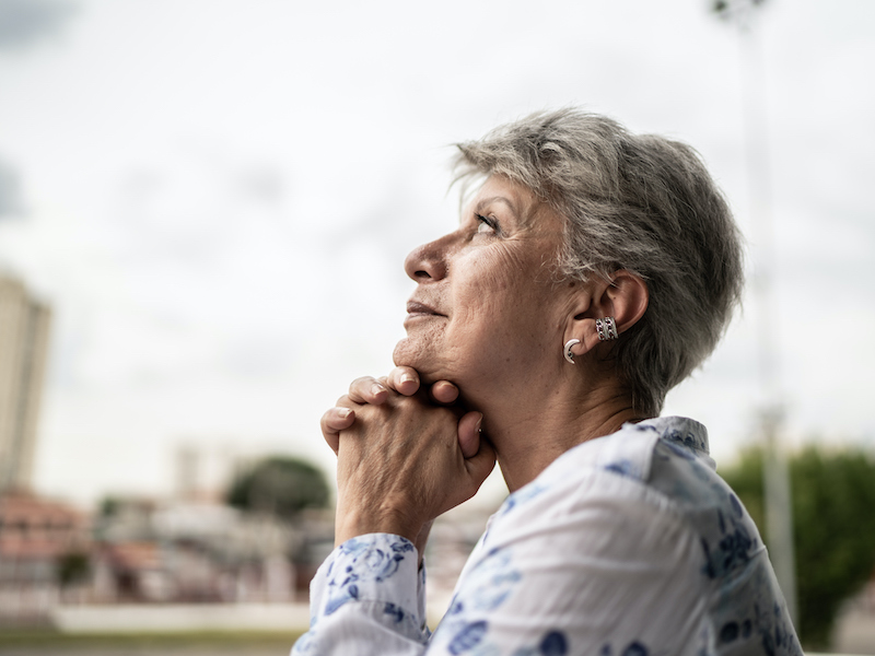 Contemplative senior woman looking away outdoors wondering about hearing loss.