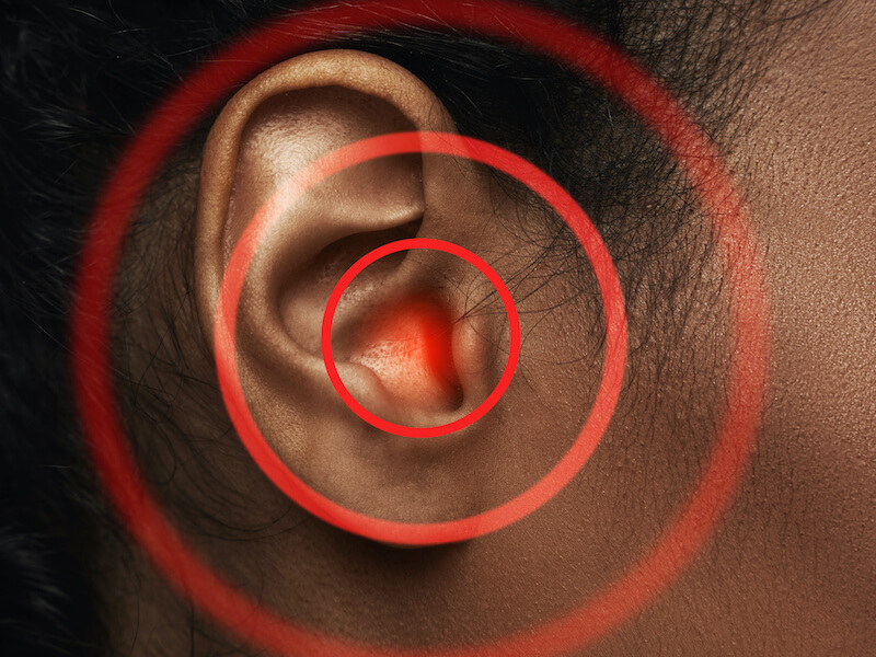 Close-up of woman's ear with red source of pain from tinnitus.