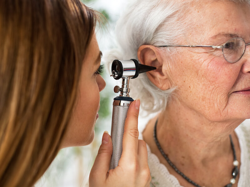 Hearing specialist holding otoscope and examining ear of senior woman