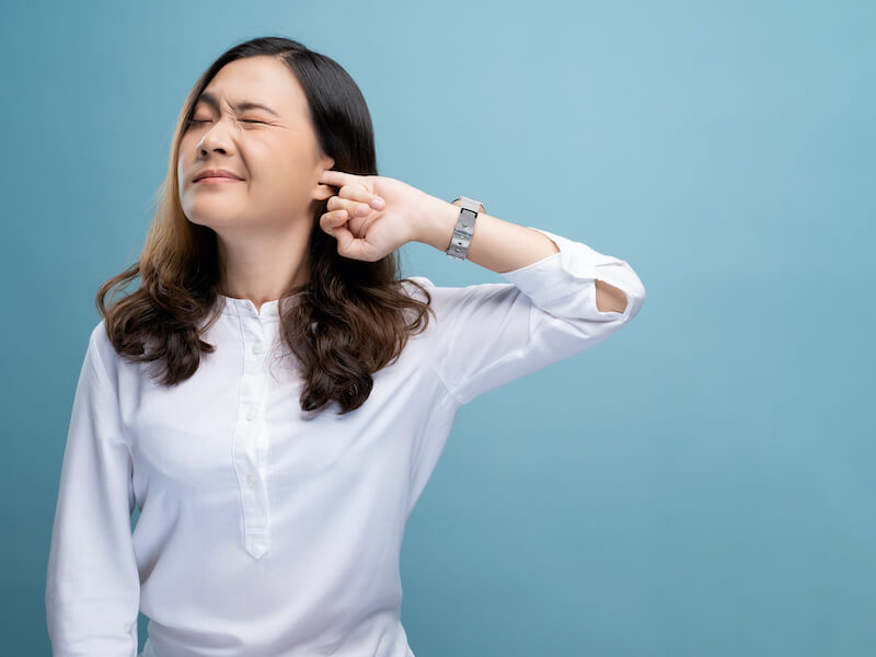 Woman putting a finger into her ear trying to release ear wax blockage.