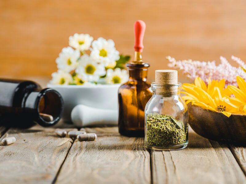 Homeopathic herbs and flowers in mortar and pestle with tincture and medicine bottles on a wooden table