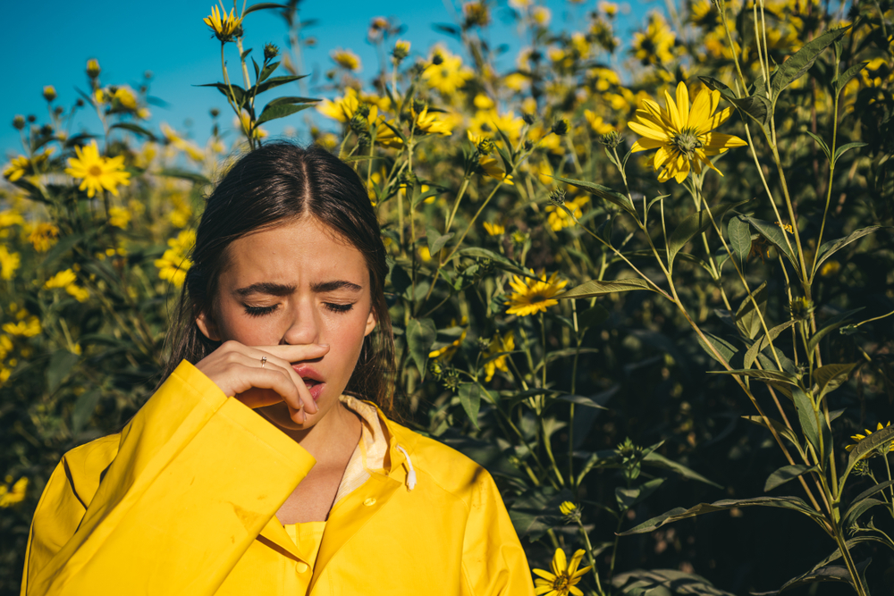Woman is blowing her nose near flowers in bloom.