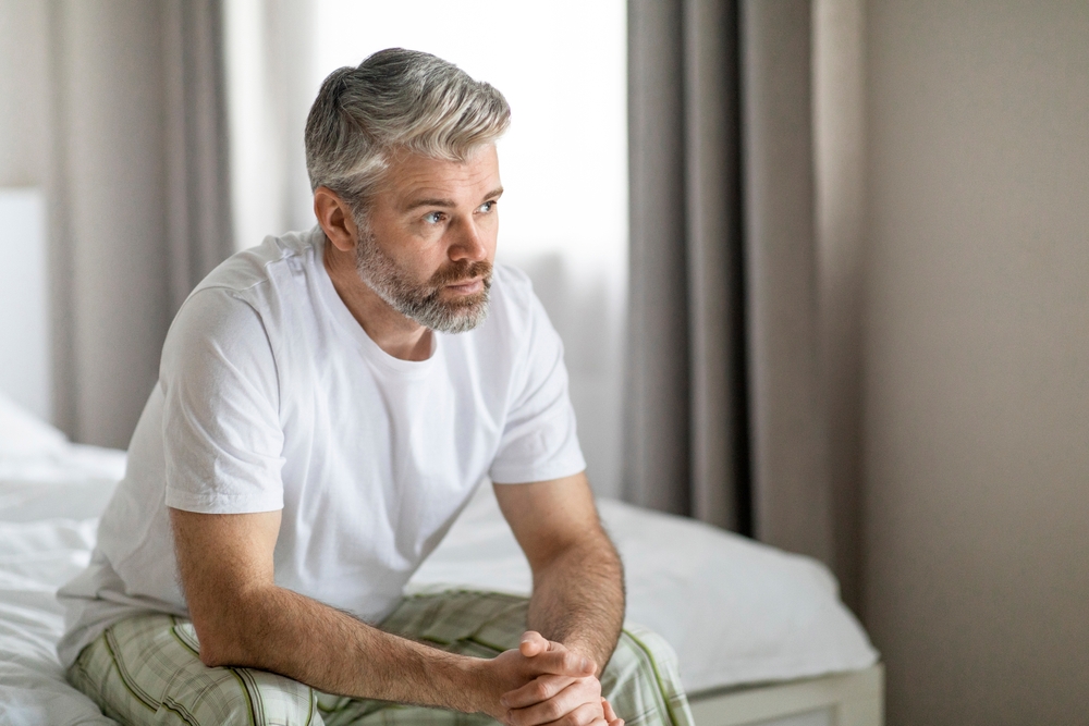 man wearing pajamas sitting on bed at home.