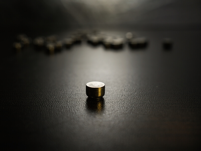 Used hearing aid batteries piled on a table with one rechargeable hearing aid battery in the foreground.