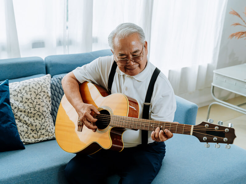 Man playing acoustic guitar on a couch to improve his hearing.