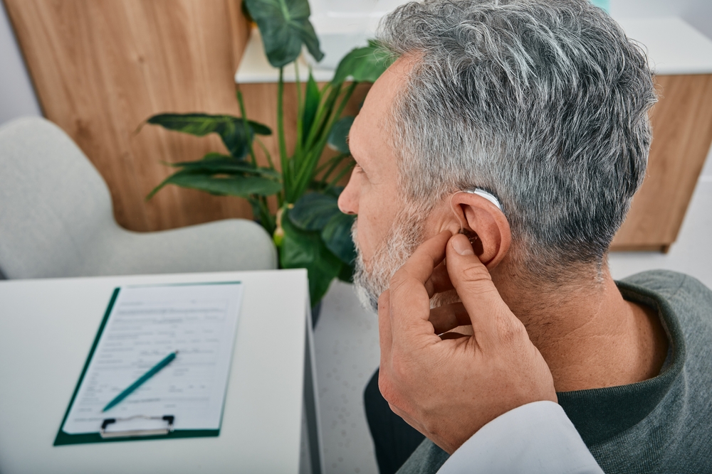 Audiologist fits a hearing aid on man.