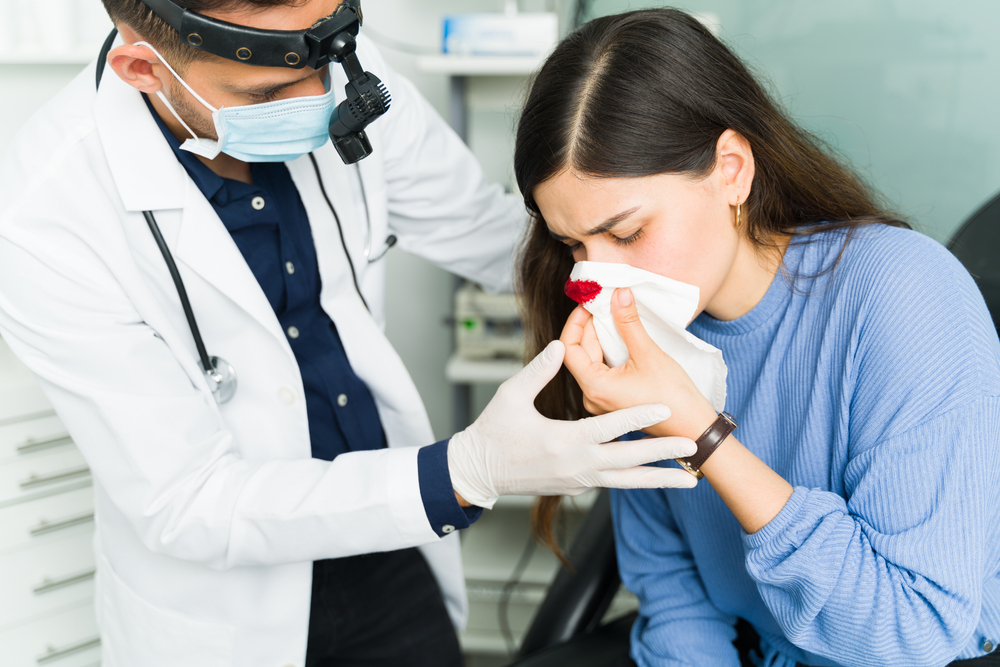 otolaryngologist trying to stop a nosebleed of a female patient.