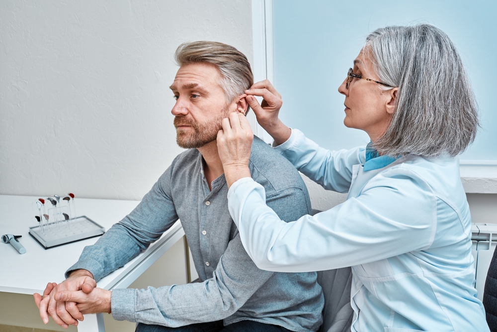 Hearing aid specialist fitting hearing aid into patient's ear.