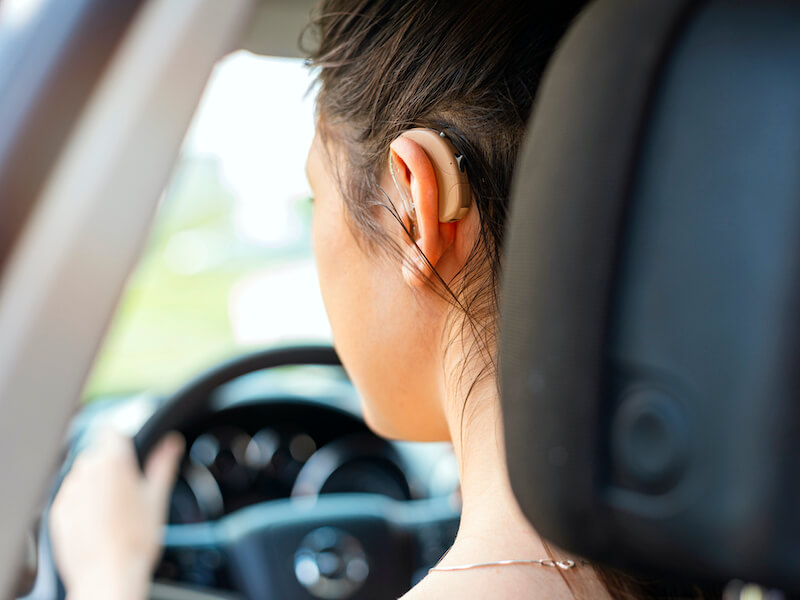 Woman with dark hair pulled back to show her wearing a hearing aid while driving