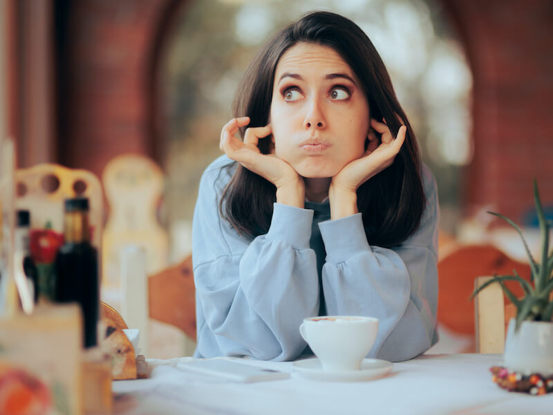 Annoyed woman worried about hearing loss with dark hair plugging her ears in a very noisy restaurant.