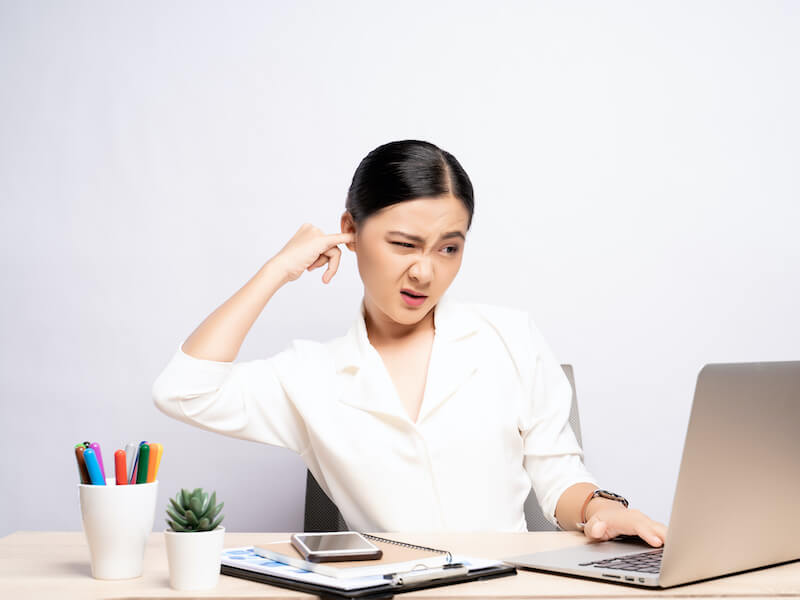 Woman with itchy ear putting a finger into her ear at office isolated white background