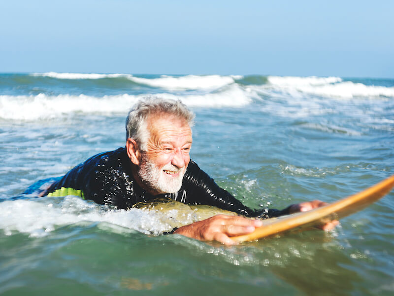 A senior man on a surfboard at risk for swimmer's ear.