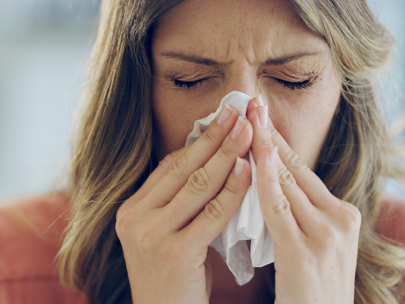 A woman feeling ill from chronic sinusitis who is blowing her nose with a tissue.