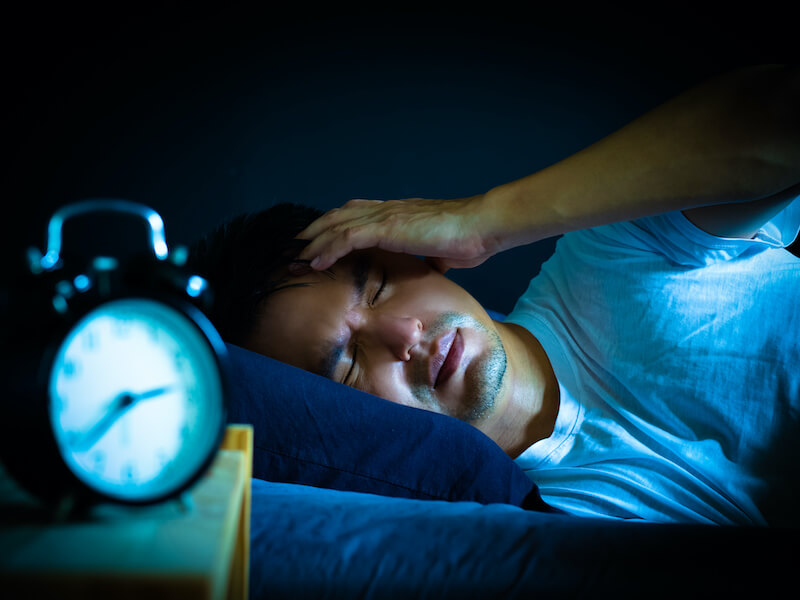 Man in bed at night suffering insomnia from severe tinnitus and ringing in the ear.