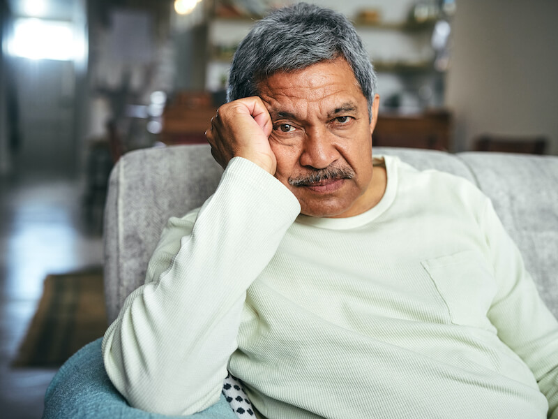 A senior man suffering from hearing loss looking unhappy on the sofa at home