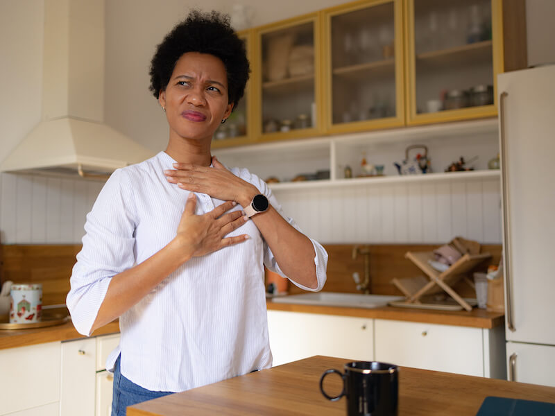Worried black woman holding her chest in pain from persistent heartburn at home.