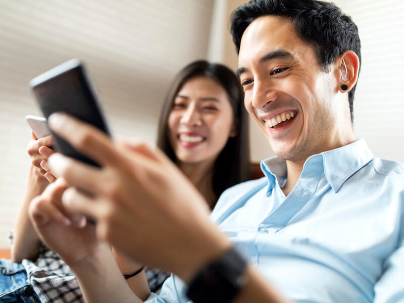Man wearing hearing aids happily using a cell phone.
