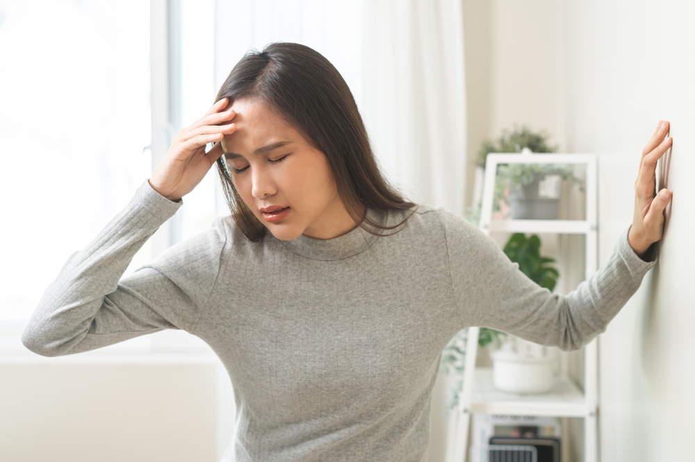 Dizzy woman has difficulty standing up, leaning on wall at home.