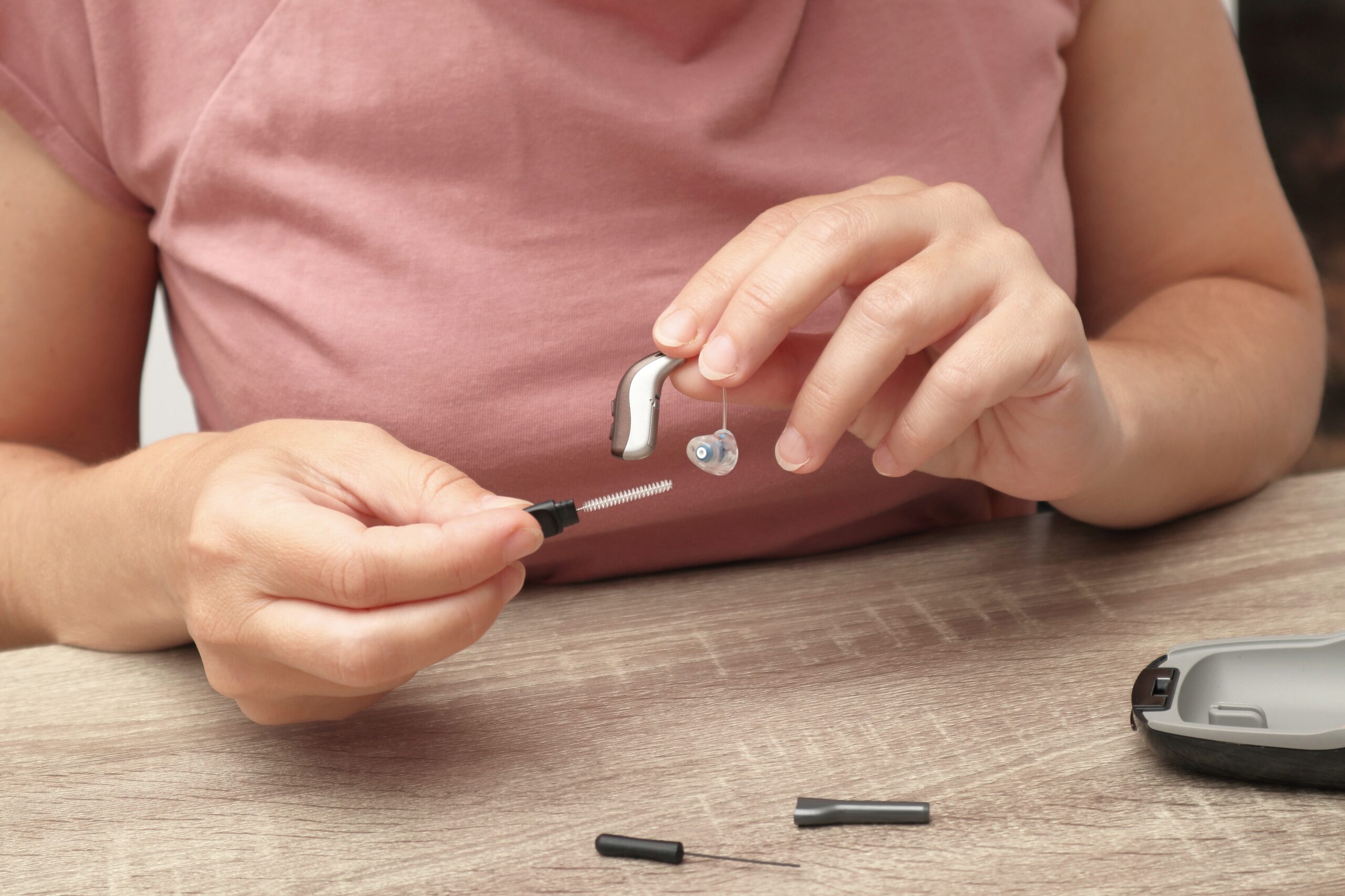 Woman holding a receiver-in-canal hearing aid and cleaning brush near its charging case, from Illini Hearing in Champaign and Mahomet, IL