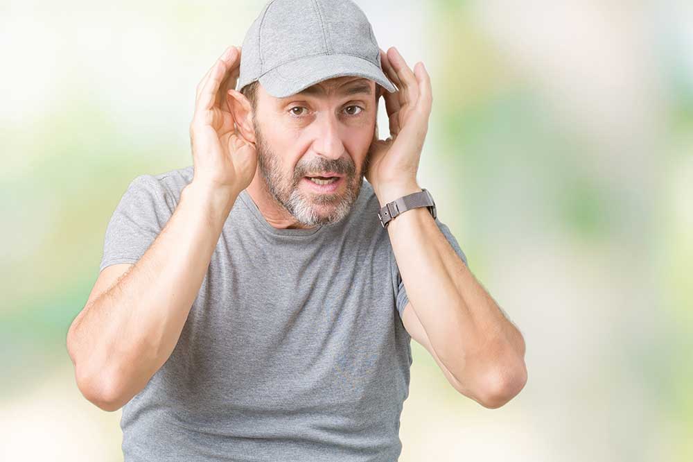 Man in a gray cap cupping his hands around his ears to hear, like when hearing aids sound uneven, at My Hearing Aid Place in Richmond Hill, GA