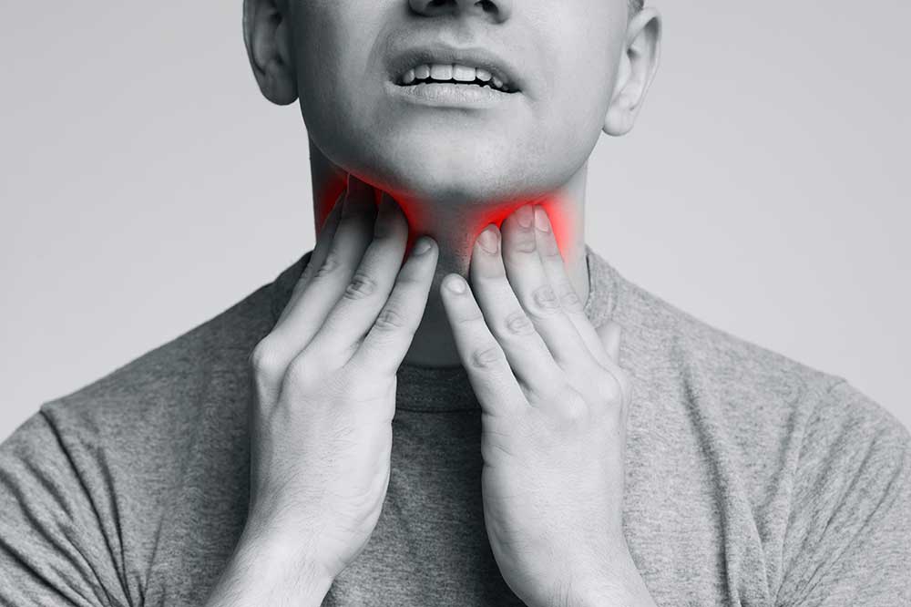 Black-and-white close-up of a man’s hands on his throat with a red glow, showing a lump-in-the-throat feeling, at ENT Associates of Fresno, CA