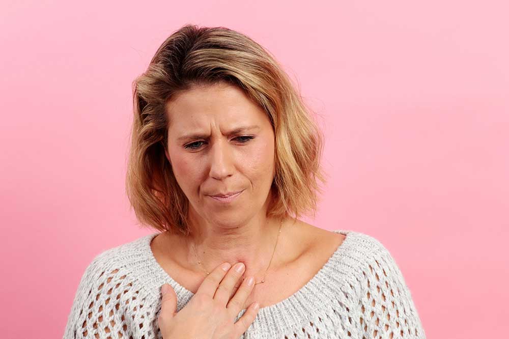 Woman in a white sweater with her hand at her throat, uneasy over a lump-in-the-throat feeling, at Coastal Ear, Nose & Throat in Savannah, GA