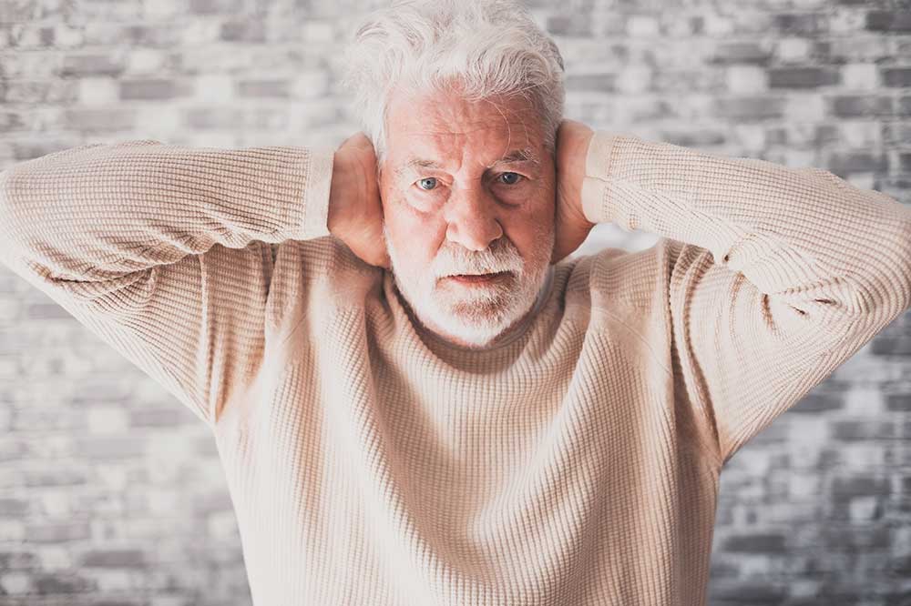 Older man covering both ears, illustrating ear fullness and muffled hearing, from The Hear Care Center in Stuart, FL