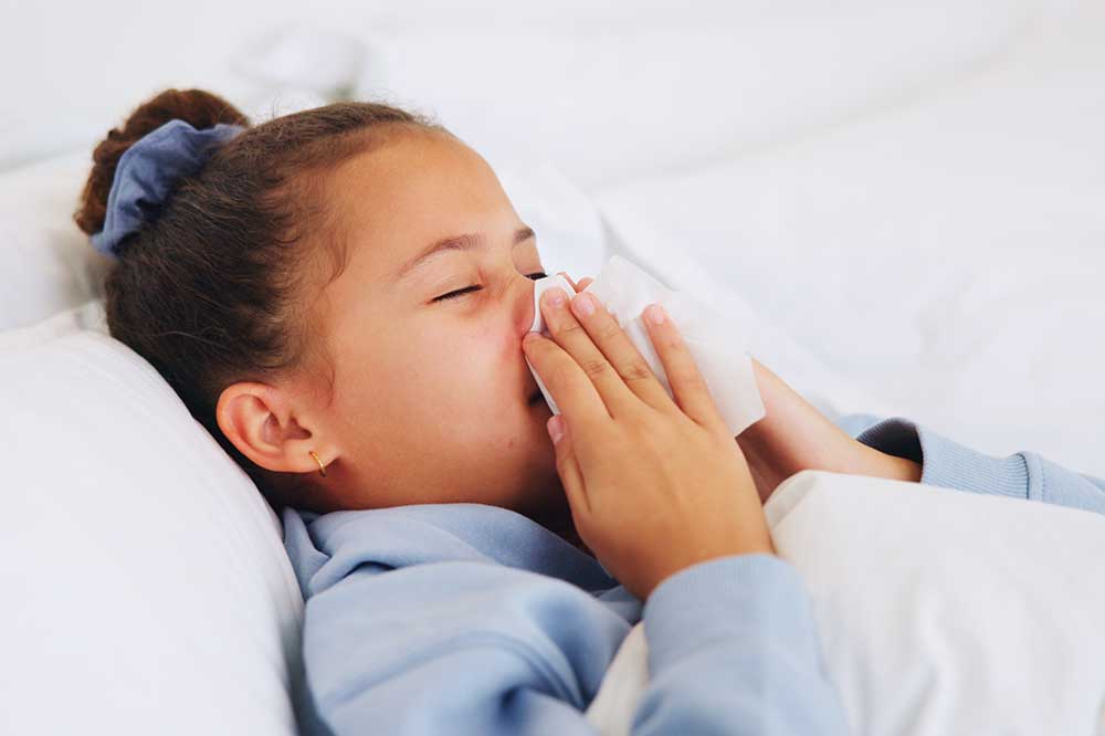 Young girl in bed blowing her nose during a sinus infection, a common concern at Coastal Ear, Nose & Throat in Savannah, GA